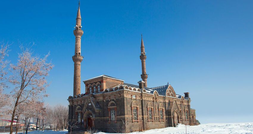 Una grande moschea in pietra con due minareti si erge in un paesaggio coperto di neve sotto un cielo azzurro e limpido.