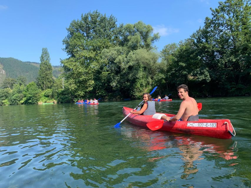 Un hombre y una mujer en un kayak rojo sonríen a la cámara durante un viaje en grupo de WeRoad en un río soleado.