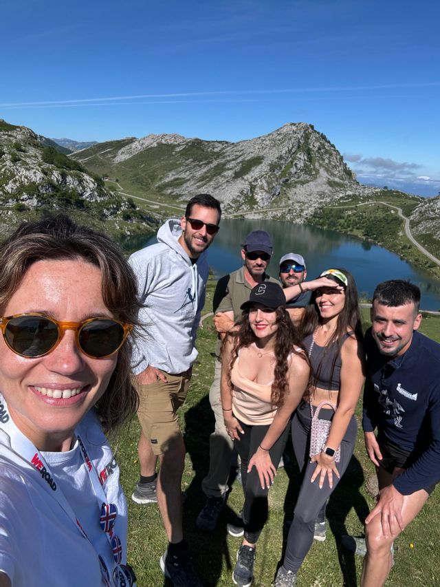 Un viaje en grupo de WeRoad posa para una selfie en un día soleado con un lago de montaña de fondo.