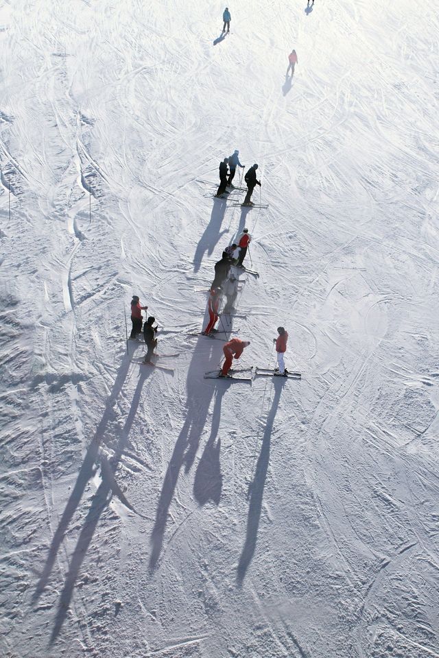 Un gruppo WeRoad di sciatori, visti dall'alto su un pendio innevato, proietta lunghe ombre sulla neve.