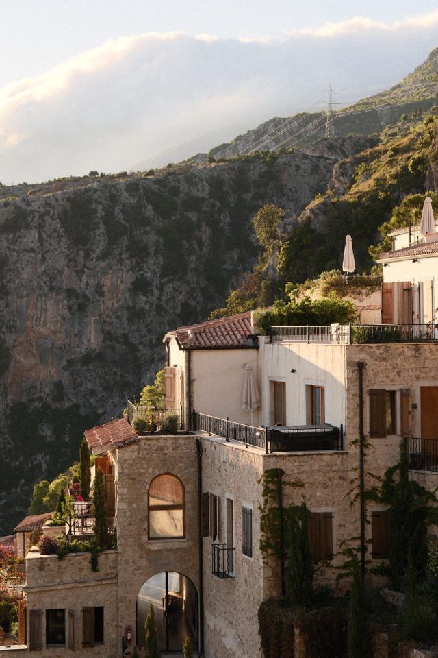 Bâtiments de pierre aux toits de tuiles et balcons, construits à flanc de montagne luxuriant et rocheux, à l'heure dorée.