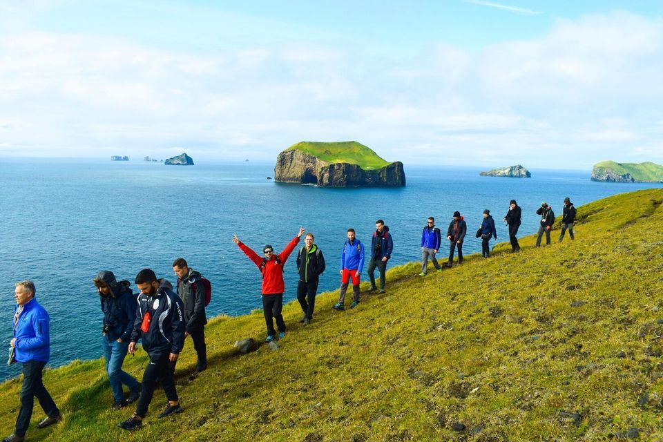 Un groupe WeRoad en randonnée sur une colline herbeuse surplombant la mer, avec de petites îles au loin.