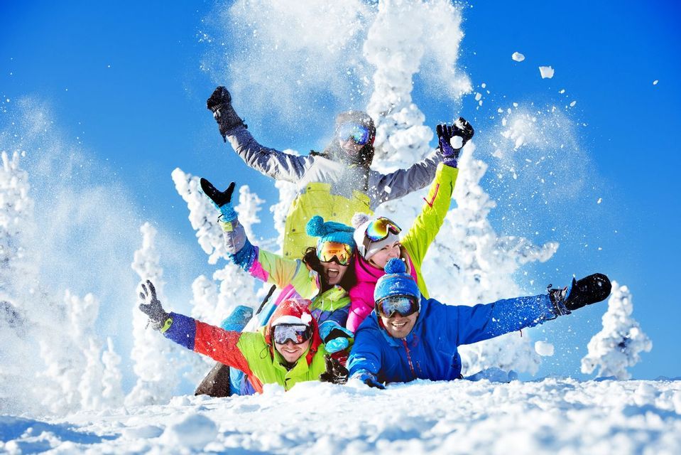 Un viaggio di gruppo WeRoad di cinque persone con abbigliamento invernale colorato che ridono e giocano insieme nella neve profonda sotto un cielo azzurro brillante.