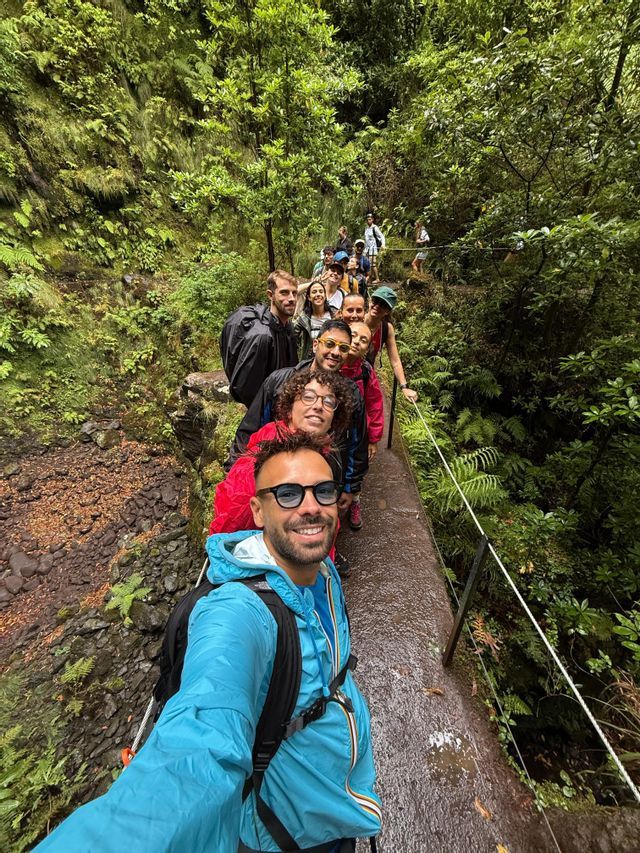 Un uomo si scatta un selfie del suo viaggio di gruppo WeRoad mentre camminano in fila lungo un sentiero stretto e bagnato in una fitta foresta verde.