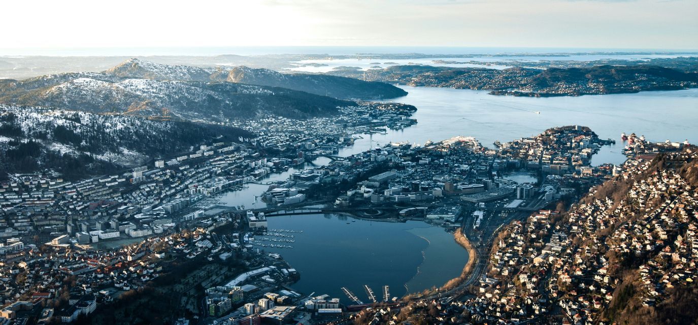 An aerial view of a coastal city nestled between snow-dusted mountains and a calm body of water leading to the sea.