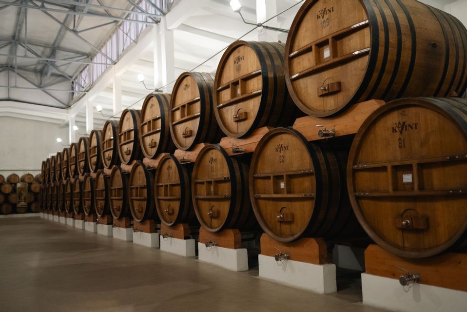 Grandi botti di legno sono disposte su due livelli in lunghe file ordinate all'interno di un luminoso magazzino di una distilleria.