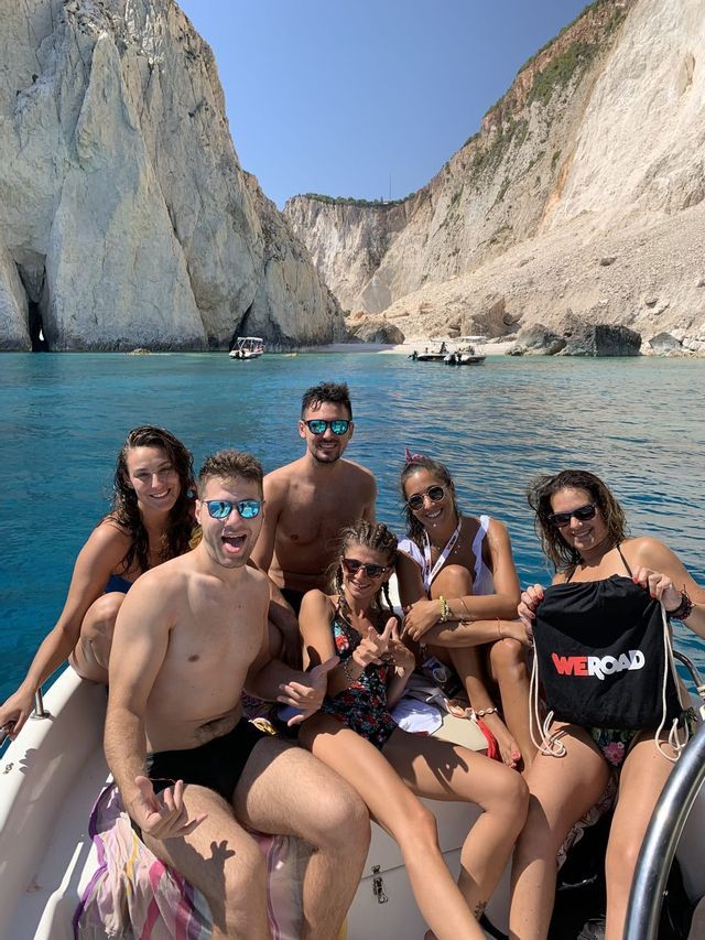 Un viaje en grupo de WeRoad con gente sonriente posando en un barco en el mar con altos acantilados blancos de fondo.