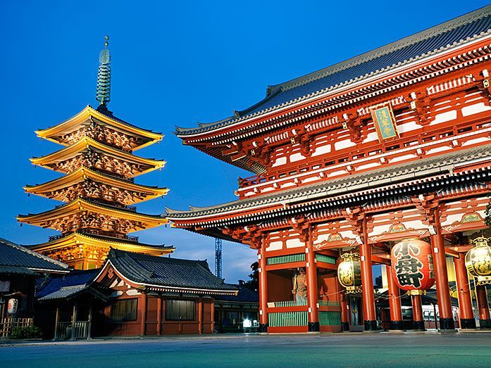 Una tradizionale pagoda giapponese e un grande cancello rosso di un tempio sono illuminati al crepuscolo sotto un cielo blu profondo.
