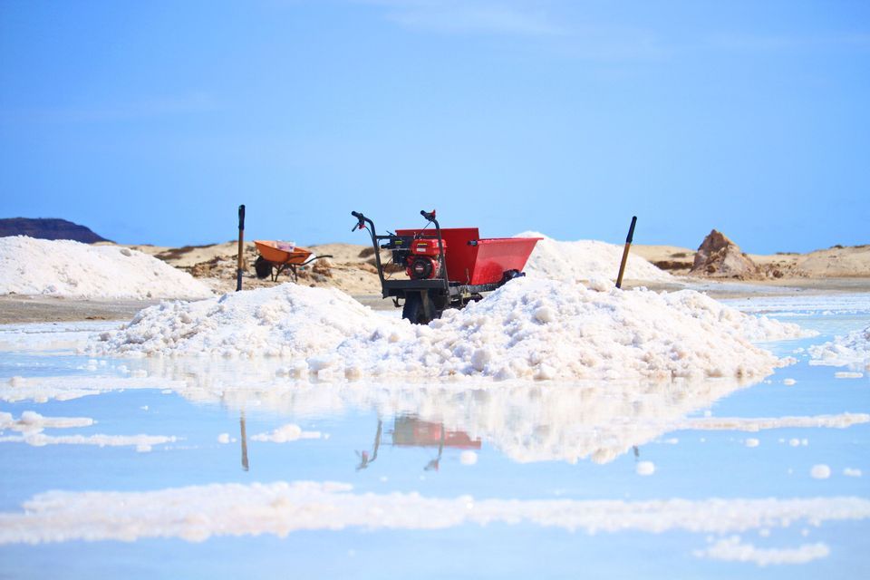 Una carriola motorizzata rossa si trova su un cumulo di sale bianco in una salina, con il suo riflesso visibile nell'acqua bassa.