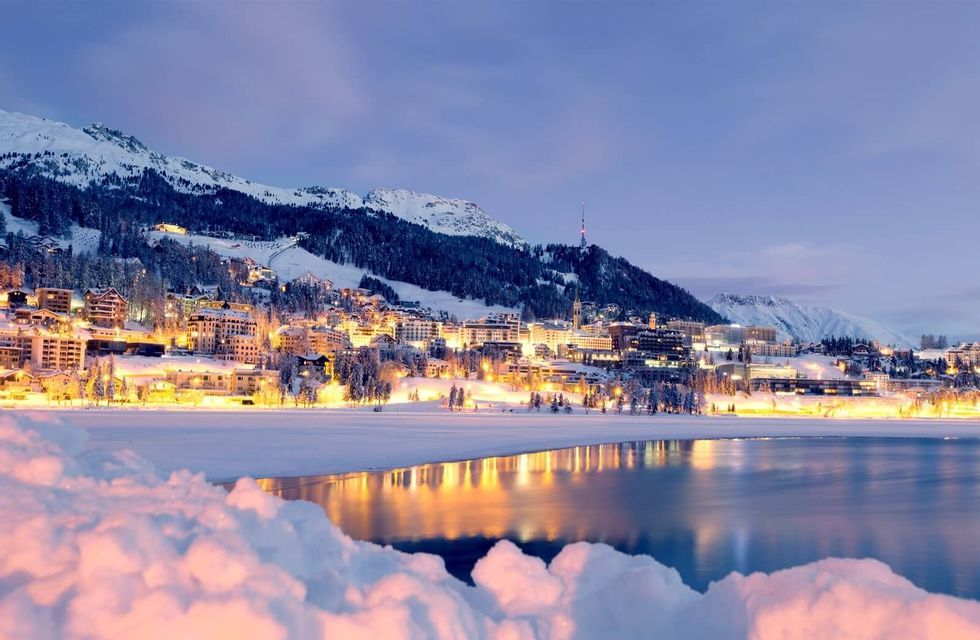 Una cittadina di montagna innevata con edifici illuminati si riflette su un lago calmo in una sera d'inverno.