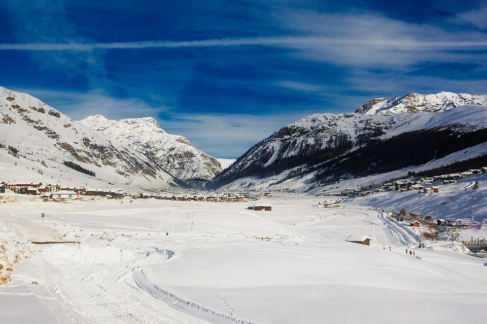 Una vasta valle innevata con un piccolo villaggio incastonato tra imponenti montagne sotto un cielo blu intenso.