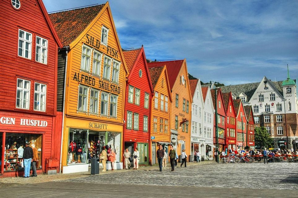 A row of colorful traditional wooden buildings with gabled roofs on a cobblestone street, with people walking in front.