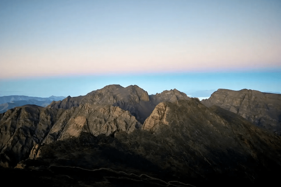 Les sommets des Rocheuses se découpent sur un ciel clair, zébré de bandes de lumière bleue et rose à l'aube ou au crépuscule.