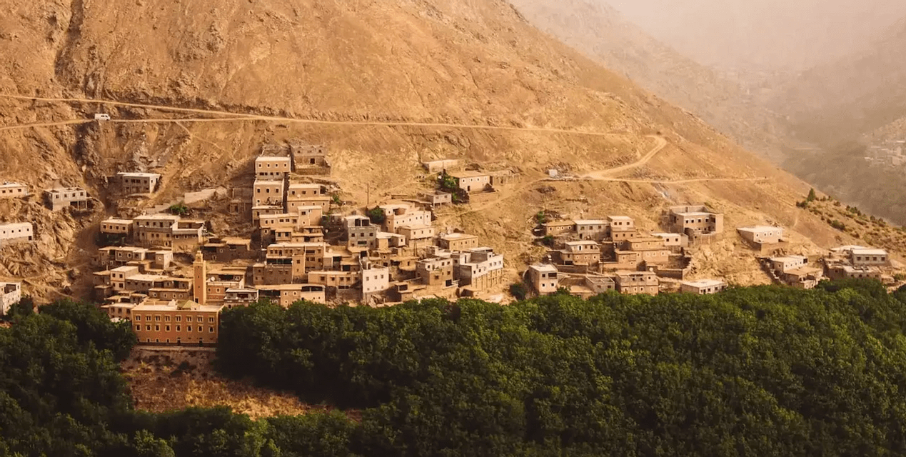 Un village de bâtiments aux tons ocres et un minaret intégré à une montagne rocheuse escarpée au-dessus d'une forêt dense et verte.