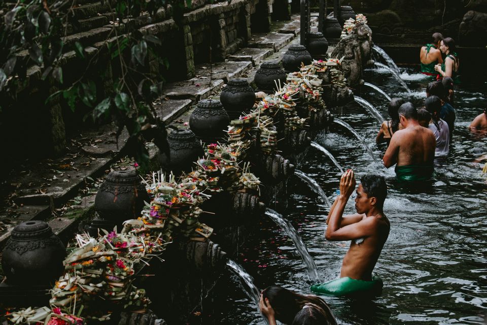 Un viaggio di gruppo WeRoad partecipa a una cerimonia di bagno rituale presso una sorgente sacra con zampilli d'acqua in pietra.