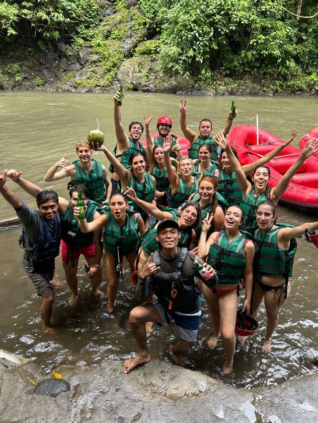 Un viaggio di gruppo WeRoad: persone in giubbotti di salvataggio sorridono e posano in un fiume, con bevande in mano e zattere rosse sullo sfondo.