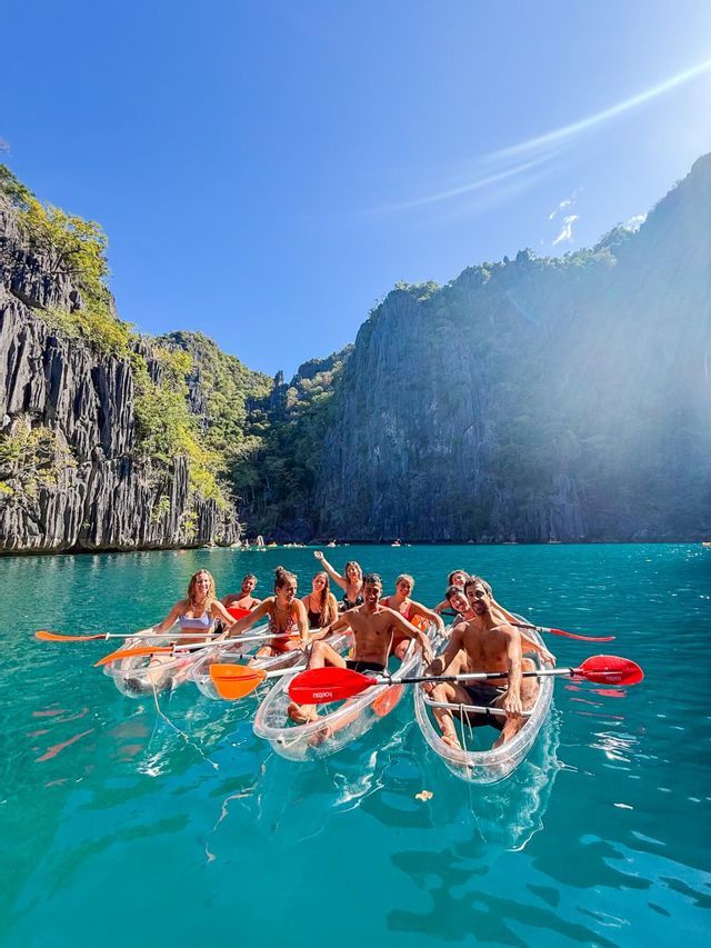 Un viaggio di gruppo WeRoad sorride per una foto in kayak trasparenti su acqua turchese accanto a scogliere rocciose.