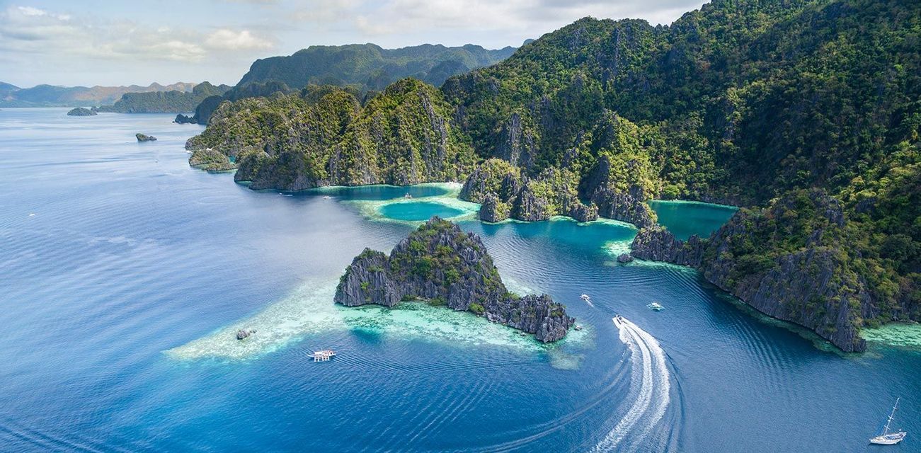Una vista aerea di barche che navigano in acque turchesi tra isole rocciose ripide e ricoperte di verde.