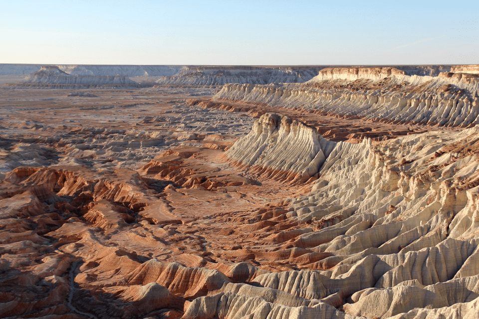 Un vasto paesaggio di formazioni rocciose erose bianche e rosse in un canyon desertico sotto un cielo sereno.