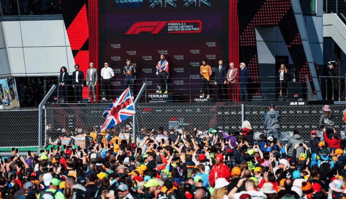 Formula 1 drivers celebrate on the podium as a large crowd cheers below at the British Grand Prix.