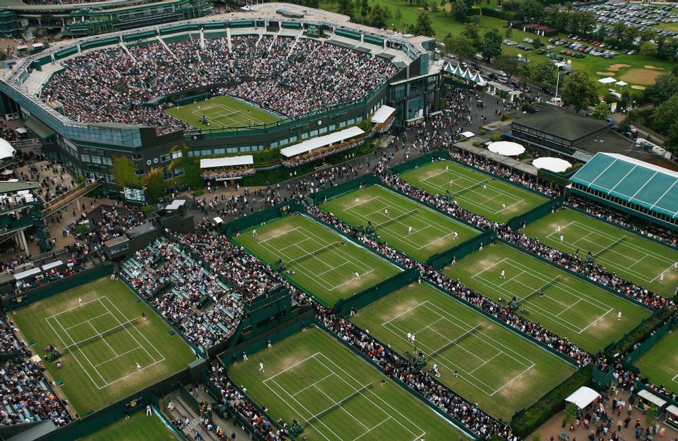 Aerial view of a large tennis complex with a main stadium and multiple courts packed with spectators during a tournament.