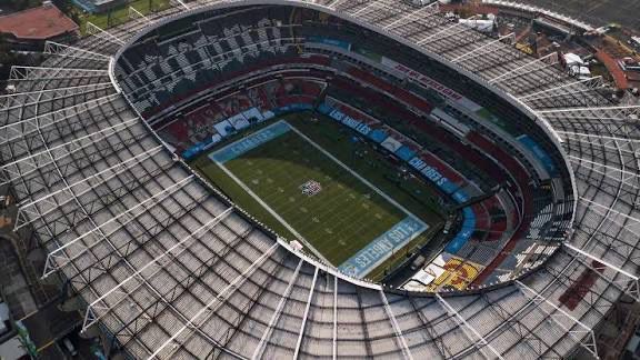 An aerial view of a large stadium with a partially open roof, revealing an American football field inside.