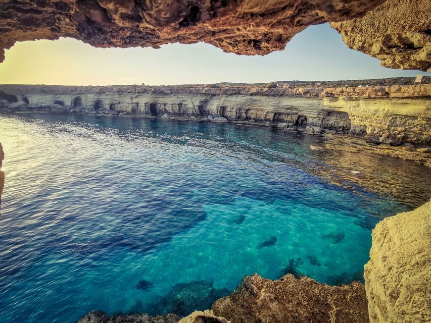 Vista dall'interno di una grotta marina su una cala con acqua turchese e scogliere rocciose.