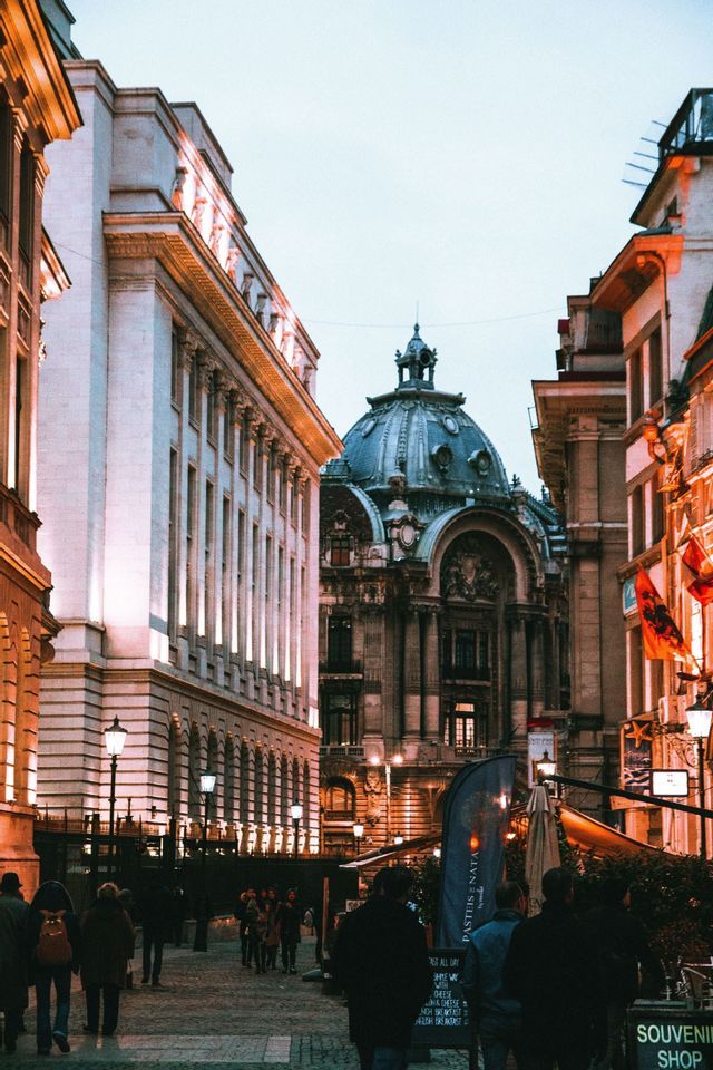 Un edificio decorato con una grande cupola si erge alla fine di una strada di ciottoli dove le persone camminano al tramonto.