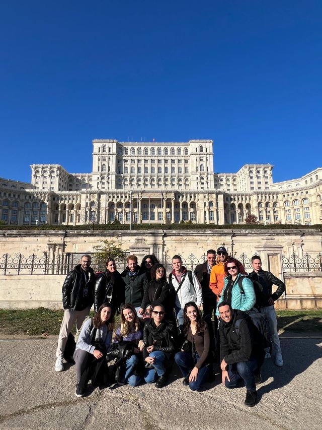 Un viaggio di gruppo WeRoad in posa per una foto davanti a un grande edificio storico sotto un cielo azzurro e limpido.