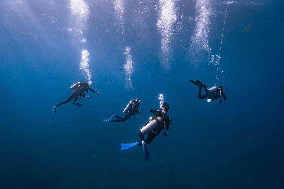 Un voyage en groupe WeRoad de quatre personnes faisant de la plongée sous-marine dans des eaux d'un bleu profond, avec des bulles d'air remontant à la surface.