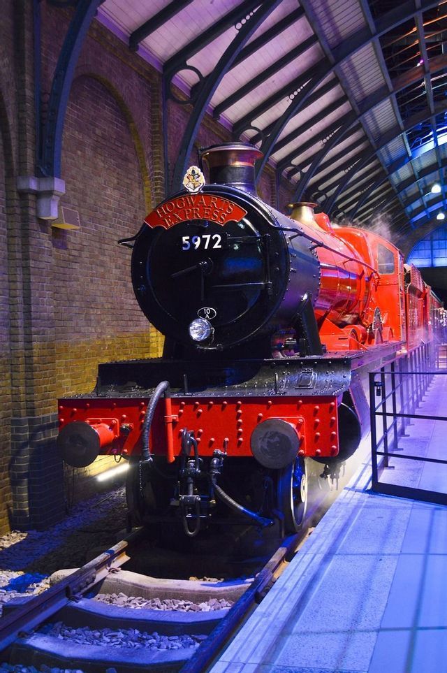 Der rote und schwarze Hogwarts Express Dampfzug, Nummer 5972, steht an einem Bahnsteig in einem Bahnhof mit Ziegelmauern.