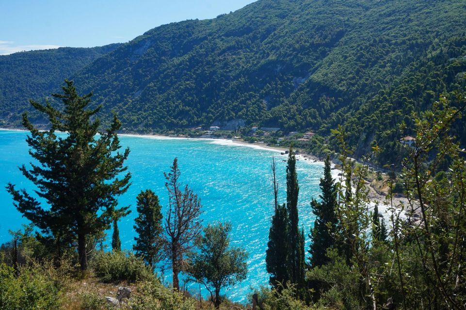 Panoramica di una costa con acque turchesi, spiaggia bianca e montagna con foresta verde.