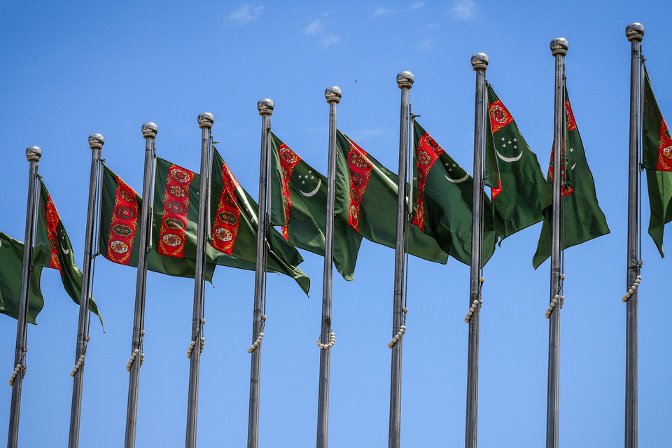 Una fila di bandiere del Turkmenistan su aste d'argento che sventolano contro un cielo azzurro e limpido.