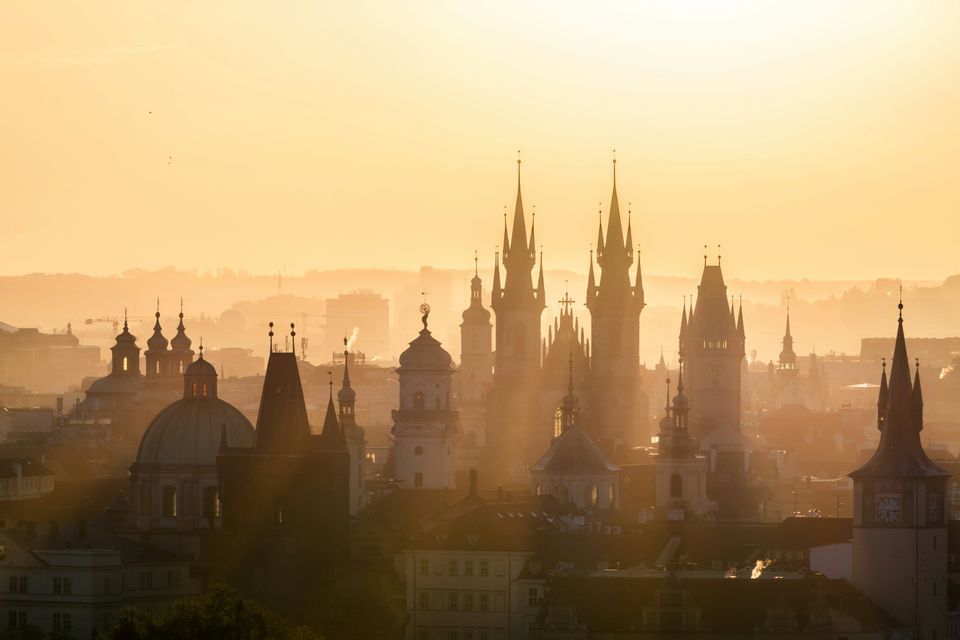 Eine Stadtkulisse aus zahlreichen Türmen und Spitzen, die sich im warmen, goldenen Licht eines diesigen Sonnenaufgangs abzeichnen.