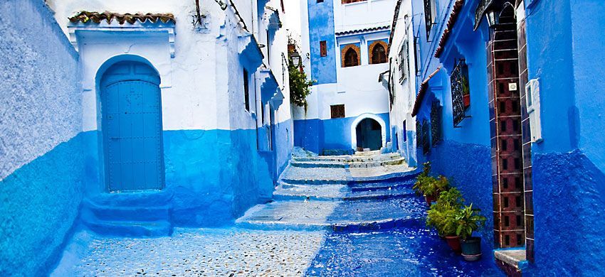 Un callejón estrecho y serpenteante de adoquines con escalones de piedra entre edificios pintados en vibrantes tonos de azul y blanco.