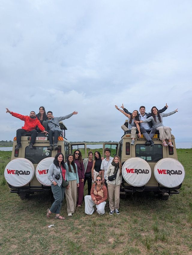 Un grupo de WeRoad posa para una foto, algunos de pie y otros sentados encima de dos vehículos de safari en un campo de hierba.