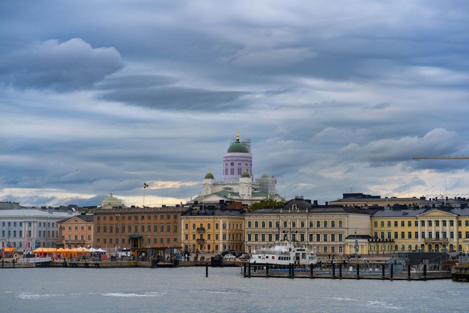Eine Stadtsilhouette mit einem großen Dom und farbenfrohen Gebäuden, vom Wasser aus unter bewölktem Himmel gesehen.