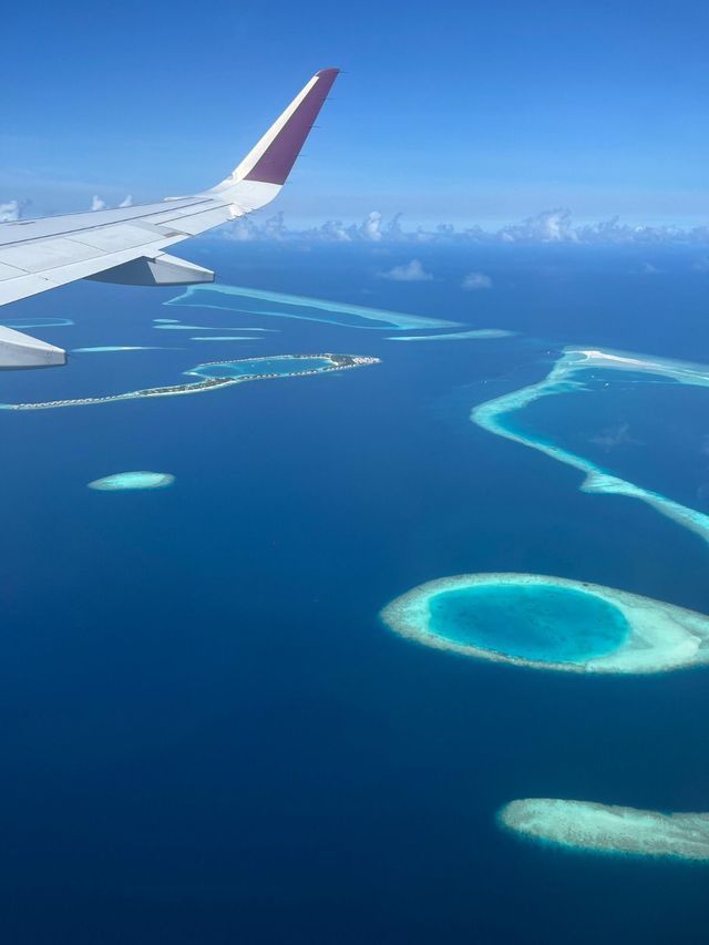Vista aerea dall'aereo, con l'ala sopra atolli tropicali e lagune turchesi in un vasto oceano blu.