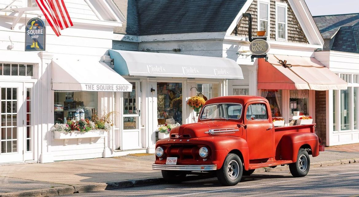Un furgoncino rosso d'epoca è parcheggiato su una strada di fronte a vetrine bianche con tende da sole.
