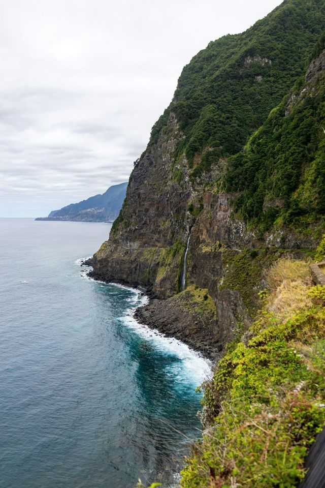 Una cascata si getta giù da una ripida scogliera verdeggiante nell'oceano, con le onde che si infrangono contro la costa rocciosa sottostante.