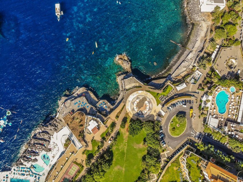 Una vista aerea, dall'alto, di un resort costiero con piscine e parchi verdi che costeggiano un oceano blu intenso.