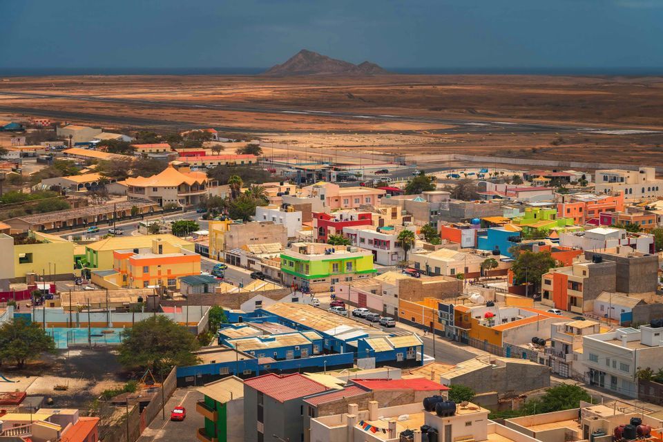 Vue en hauteur d'une ville colorée avec des bâtiments bas dans un vaste paysage aride avec une montagne à l'horizon.