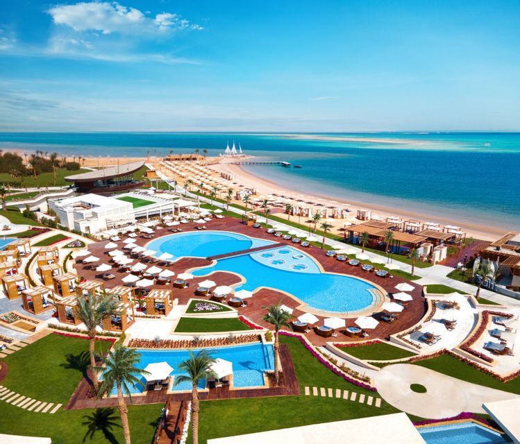 Una vista aerea di un resort di lusso sulla spiaggia con diverse piscine e palme, accanto a una spiaggia sabbiosa e all'oceano.