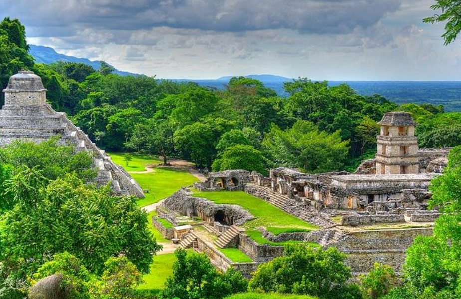 A panoramic view of stone temple ruins and pyramids surrounded by a dense green forest.