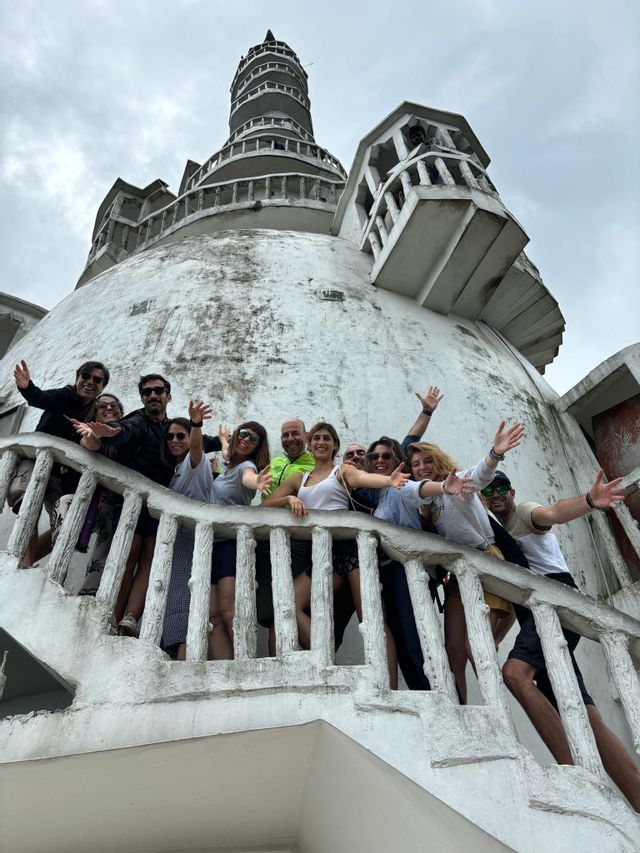Eine WeRoad-Gruppe auf Reisen posiert und winkt von der Treppe eines großen weißen Gebäudes mit Kuppel unter einem bewölkten Himmel.