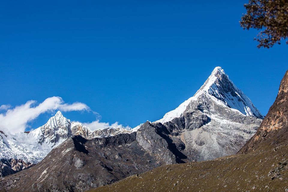 Una vetta montuosa frastagliata e innevata si staglia sopra una catena rocciosa, sotto un cielo blu limpido e vibrante.