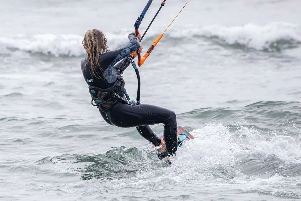 Una persona in muta nera, vista da dietro, che fa kitesurf su acqua mossa con onde.