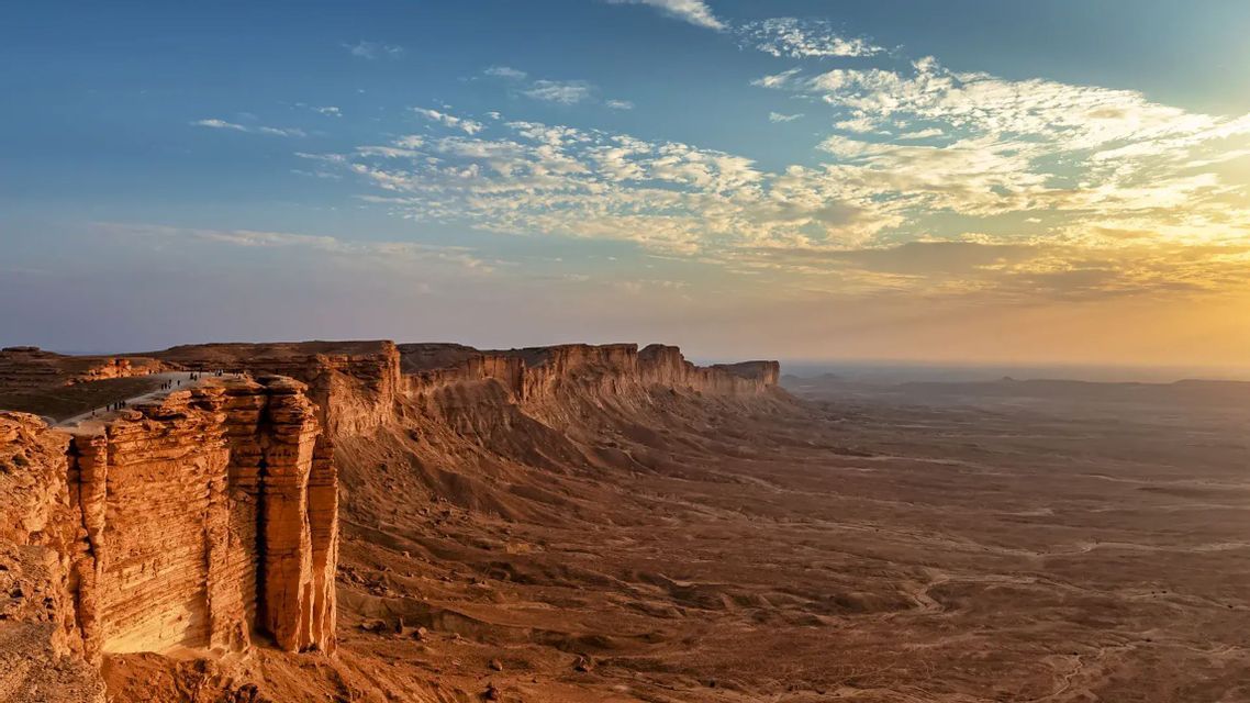 Un viaggio di gruppo WeRoad cammina lungo il bordo di una vasta scarpata rocciosa al tramonto, con vista su uno sconfinato paesaggio desertico.