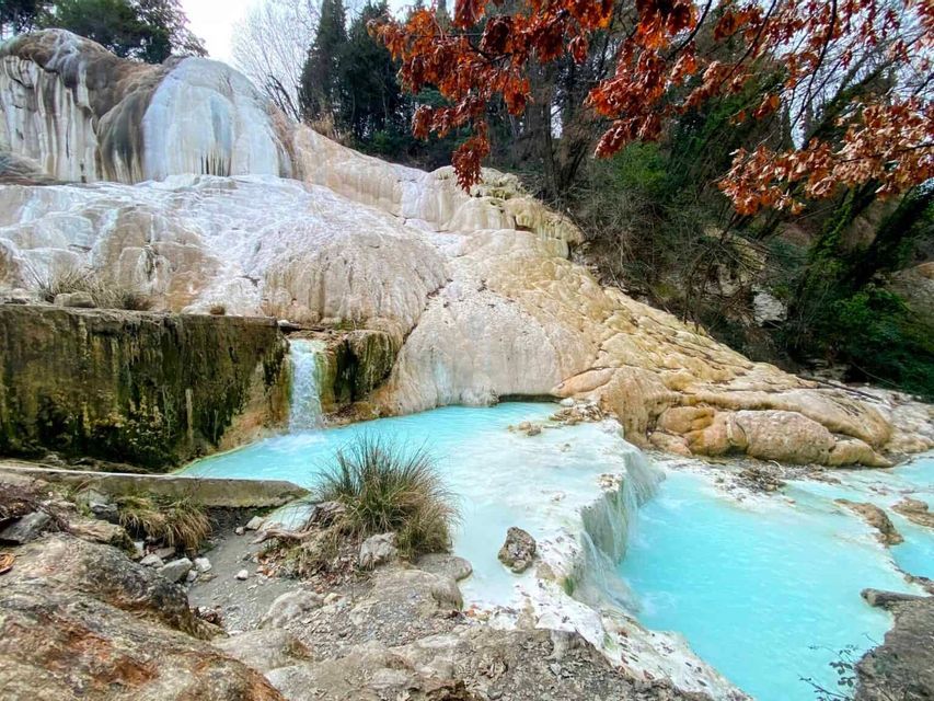 Terrazze di travertino bianco con piccole cascate che sfociano in piscine di acqua termale turchese, incorniciate da alberi con foglie autunnali.