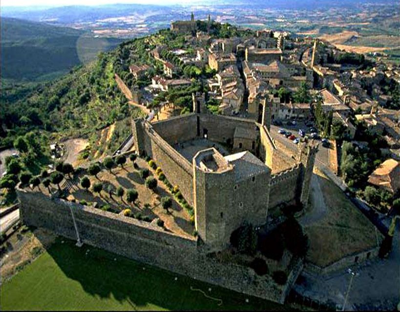 Una vista aerea di una fortezza storica e una città murata situata su una verde collina ondulata.